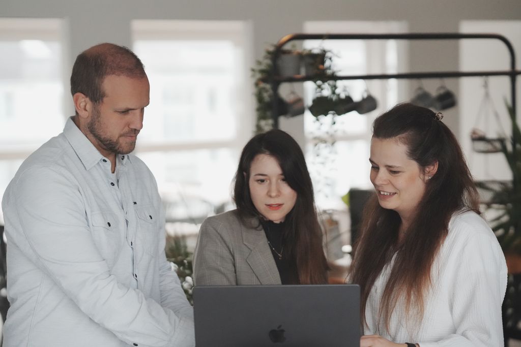 Drei Mitarbeiter arbeiten gemeinsam an einem Laptop im Büro